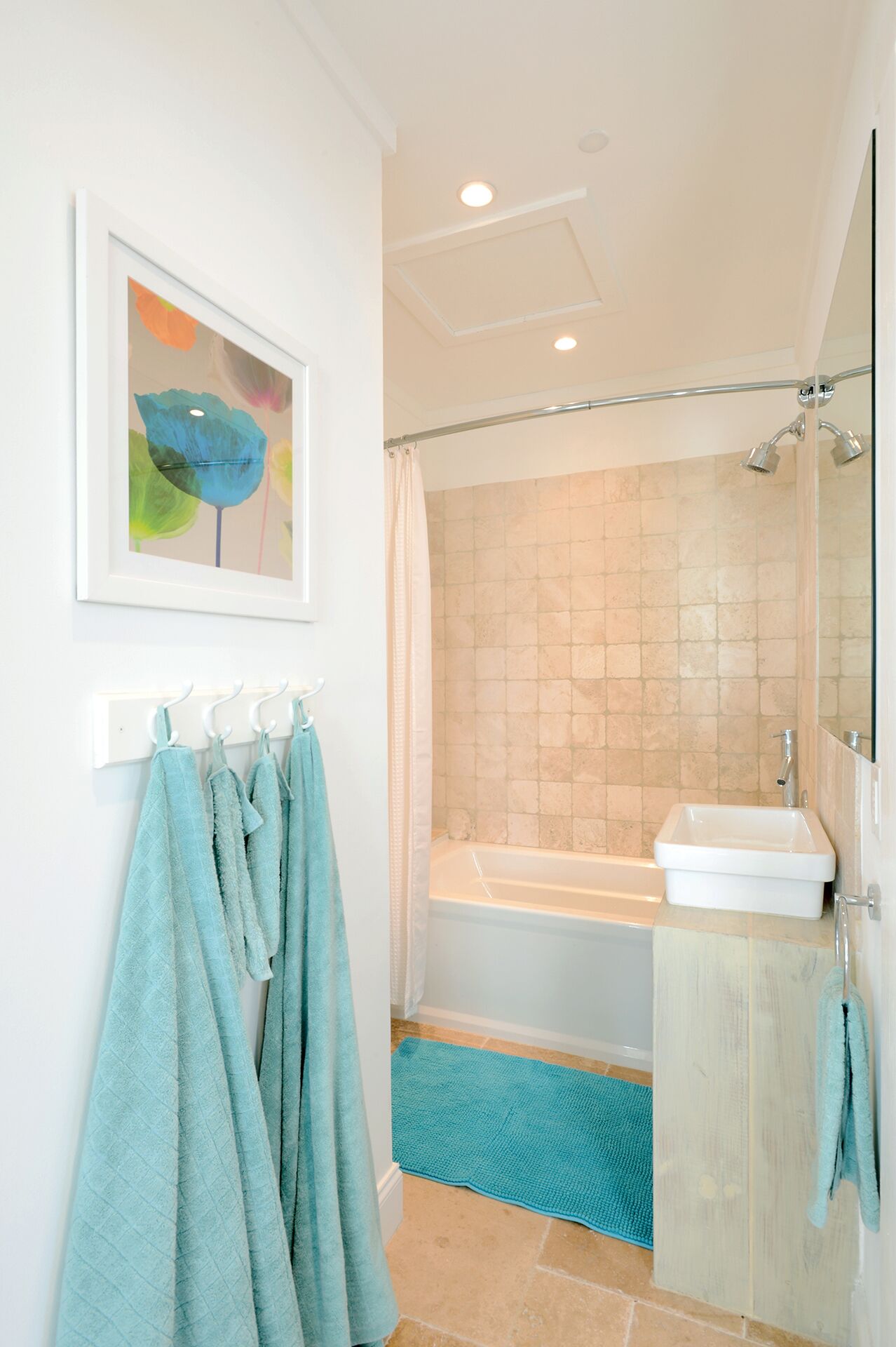 A bathroom with a bathtub, a shower, and a sink. There are towels hanging on a rack and a blue mat on the floor.