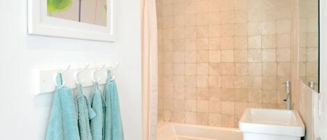 A bathroom with a bathtub, a shower, and a sink. There are towels hanging on a rack and a blue mat on the floor.