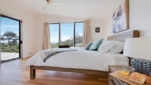 Ein Schlafzimmer mit einem großen Bett, einem Deckenventilator, Blick ins Freie und einem Frühstücksbrettchen auf dem Nachttisch.