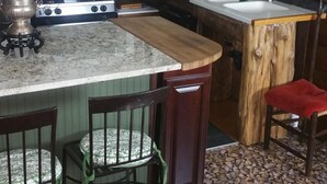 Una cocina con una isla central, microondas y estufa. Hay sillas y una mesa con un mapa.