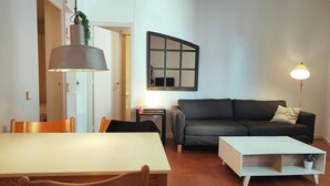 Una sala de estar con un sofá, una mesa de comedor con sillas, una lámpara y un espejo en la pared.
