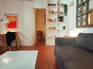 Una sala de estar con un sofá gris, una mesa blanca, una estantería y una puerta que da a otra habitación.