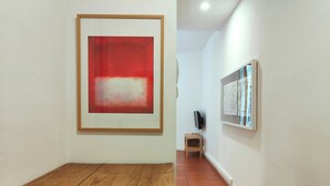 Un pasillo con un cuadro abstracto enmarcado, una mesa de madera y un televisor montado en la pared.