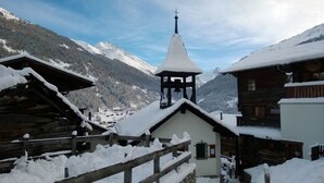 Een besneeuwd dorp met houten gebouwen, een kerk met een klokkentoren en bergen op de achtergrond.