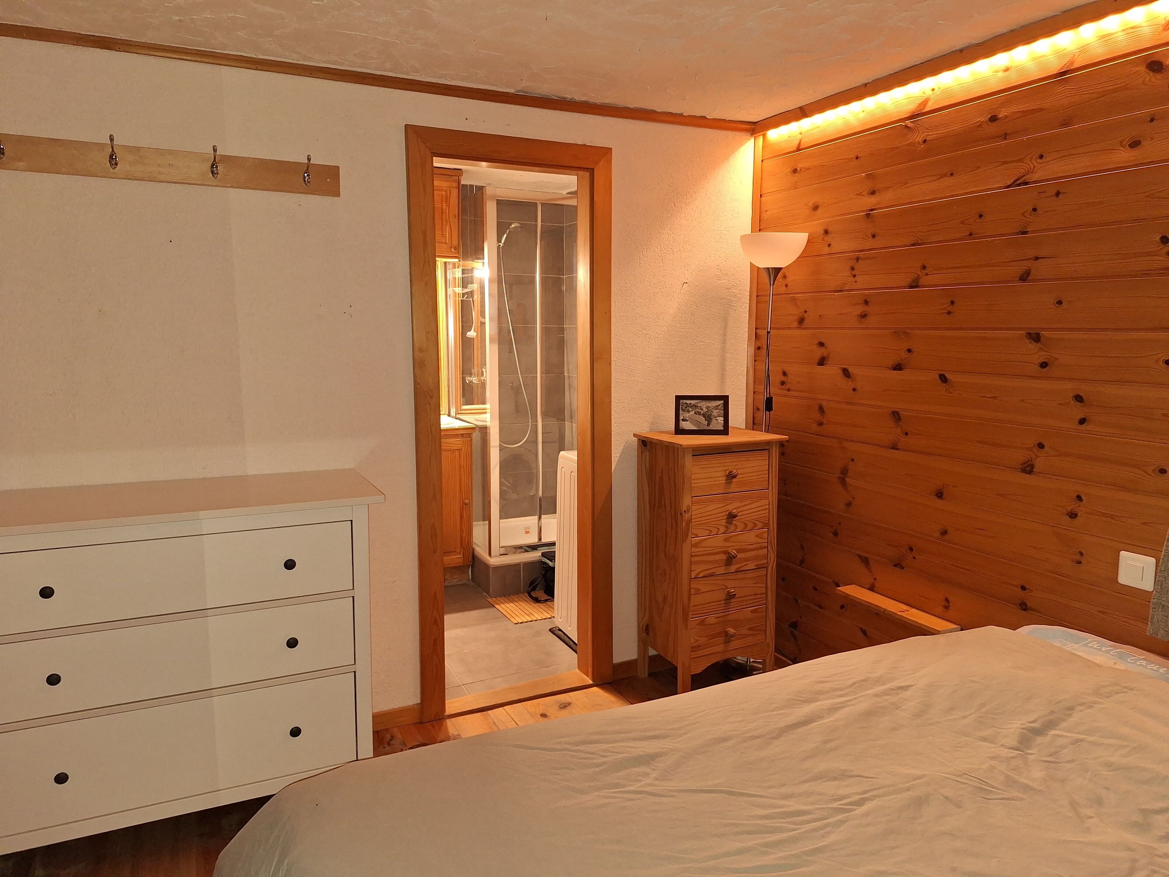 A bedroom with a wooden headboard, a bedside table with a lamp, a wooden dresser, and a white bed.