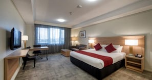 A hotel room with a large bed, a desk, a chair, a television, and a window with curtains.