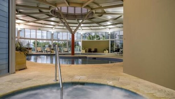 An indoor swimming pool with a clear view of the surrounding area, including a seating area and a large window.