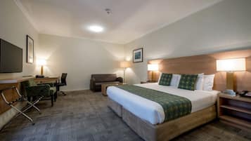 A hotel room with a bed, a desk, a chair, a sofa, and a TV.