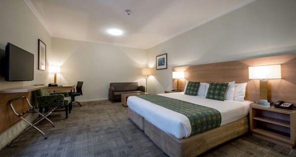 A hotel room with a bed, a desk, a chair, a sofa, and a TV.