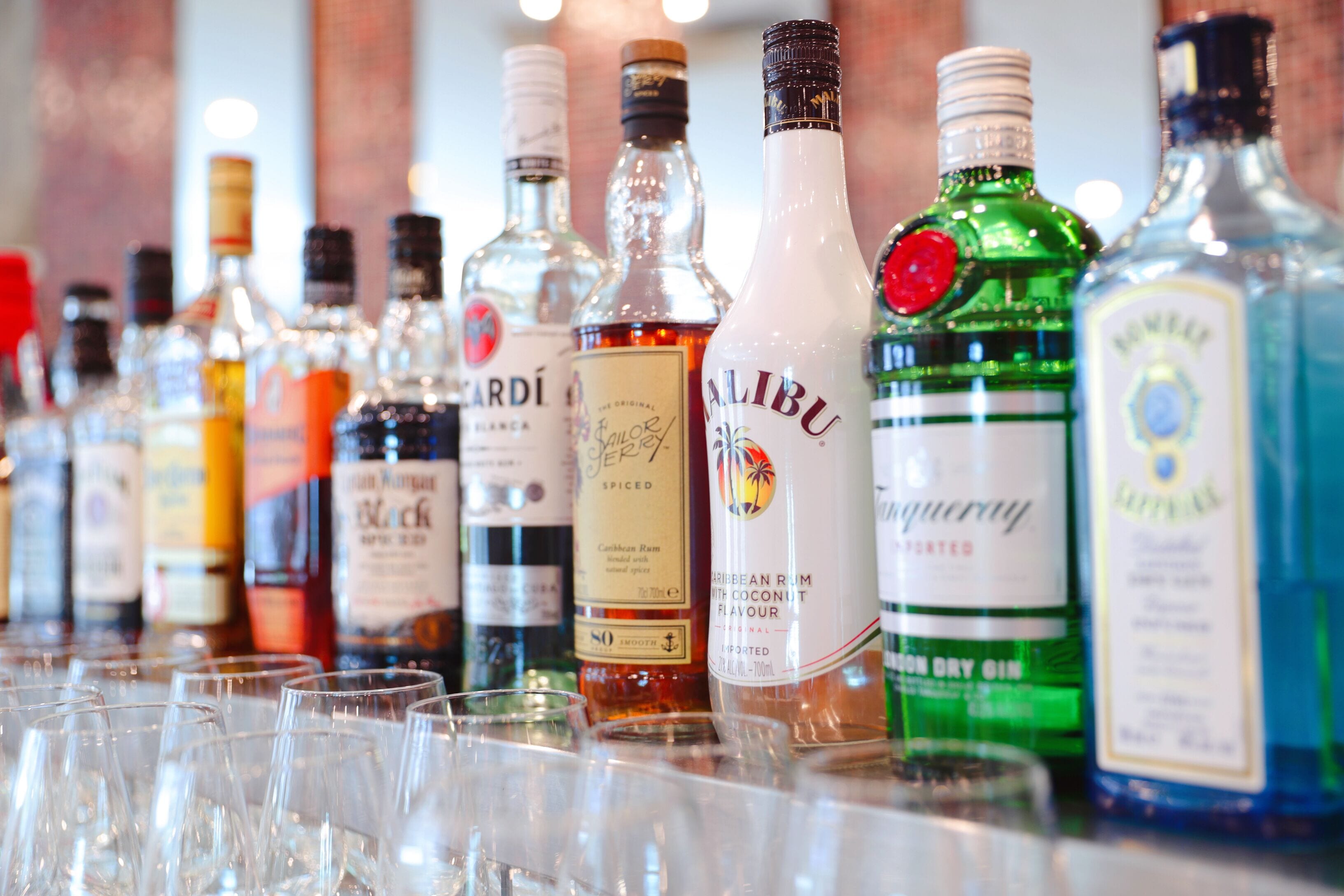 A variety of liquor bottles and empty glasses on a bar counter.