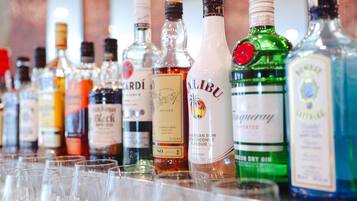 Variedad de botellas de licor y vasos vacíos sobre una barra.