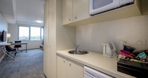 A modern kitchen with a sink, kettle, and cabinets. There is a window providing natural light and a view of the city.