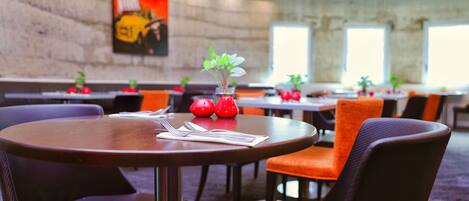 Un comedor con mesas redondas, sillas naranjas y jarrones rojos con plantas.