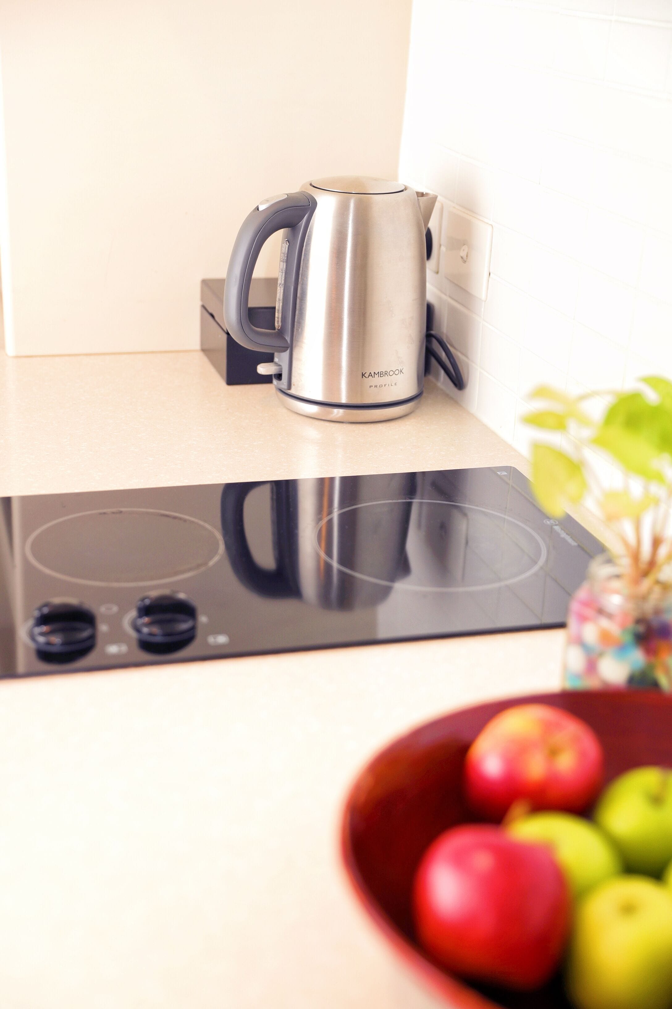 Una cocina moderna con un hervidor de acero inoxidable, una cocina por inducción y un bol de manzanas.