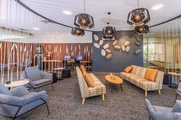 A modern lobby with a seating area, a reception desk, and a decorative wall with leaf patterns.