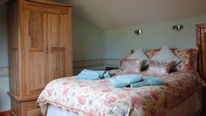 A bedroom with a floral bedspread, a wooden wardrobe, and a nightstand with a lamp. - Shiantview Cottage - Magnificent Sea Views  (Stornoway, Isle of Lewis, Scotland)