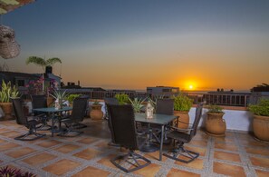 A terrace with a table and chairs, potted plants, and a sunset view. - Casa Romance Escondido (Puerto Vallarta)