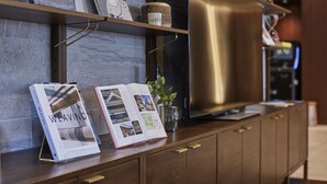 A modern kitchen with wooden cabinets, a stainless steel refrigerator, and a shelf with books and decorative items. - Iroha Grand Hotel (Matsumoto)