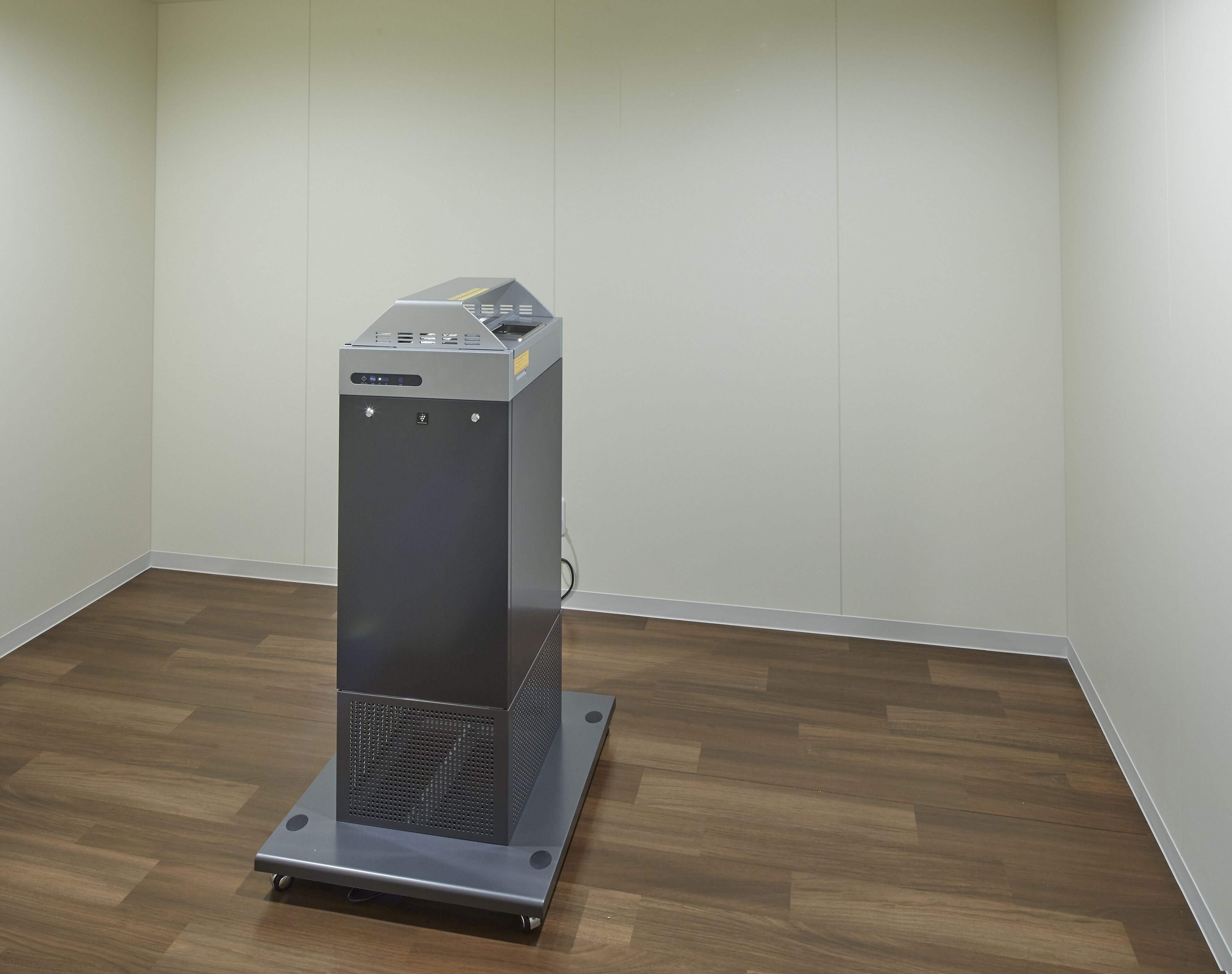 A compact, modern room with a wooden floor and white walls, featuring a small, metallic object on a stand.