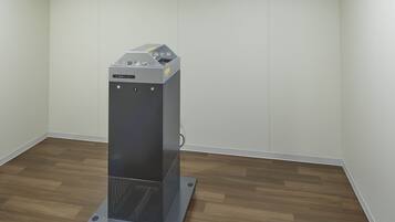 Een compacte, moderne kamer met een houten vloer en witte wanden, met een klein, metalen object op een voetstuk.