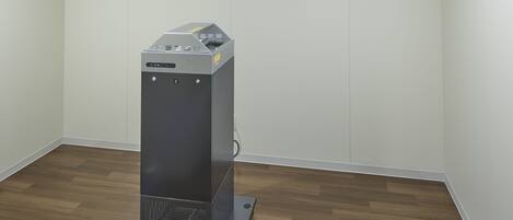 A compact, modern room with a wooden floor and white walls, featuring a small, metallic object on a stand.
