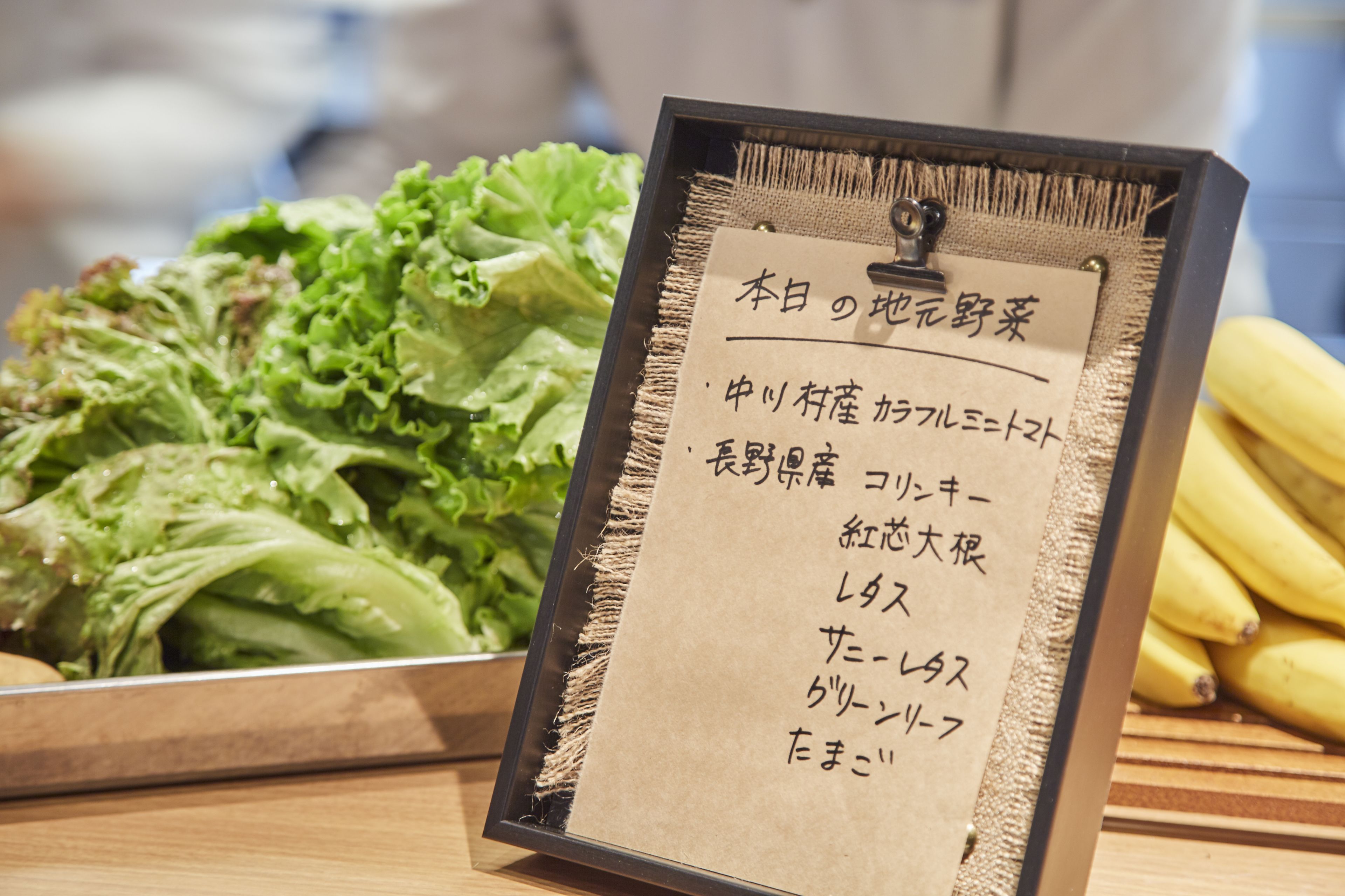 A menu board with Japanese text, a bowl of lettuce, and bananas on a table.