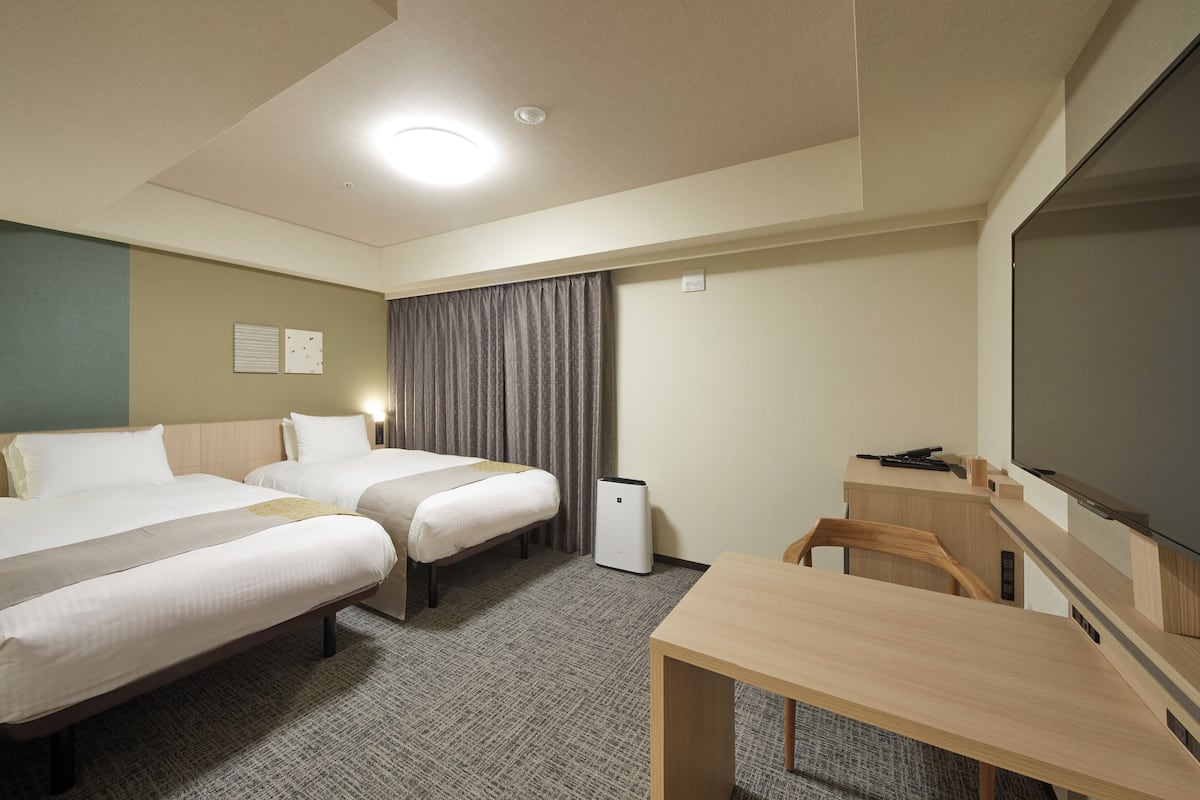 A hotel room with two beds, a desk, a television, and a small speaker.