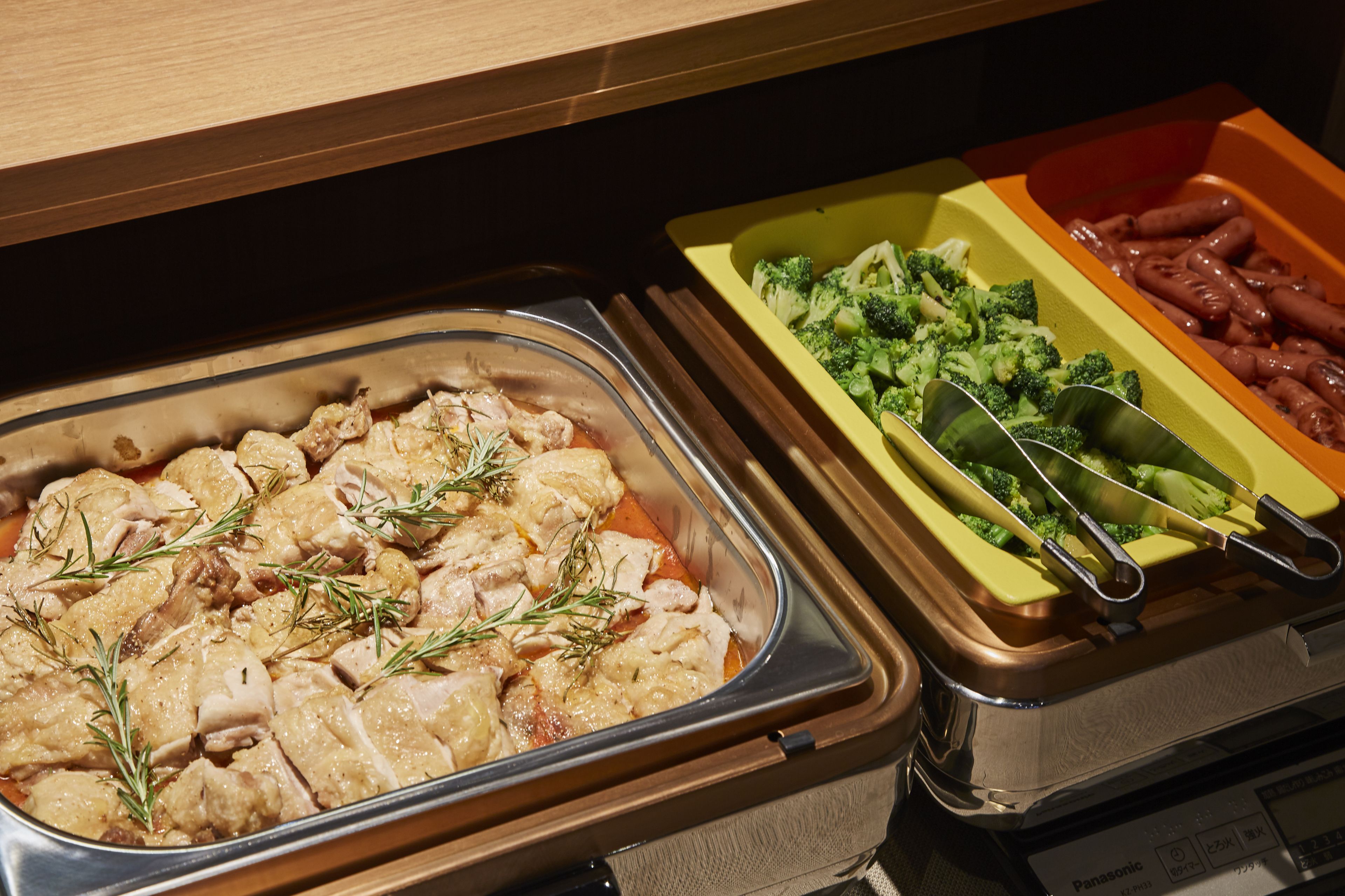 Een buffet met diverse gerechten, zoals kip, broccoli en worstjes.