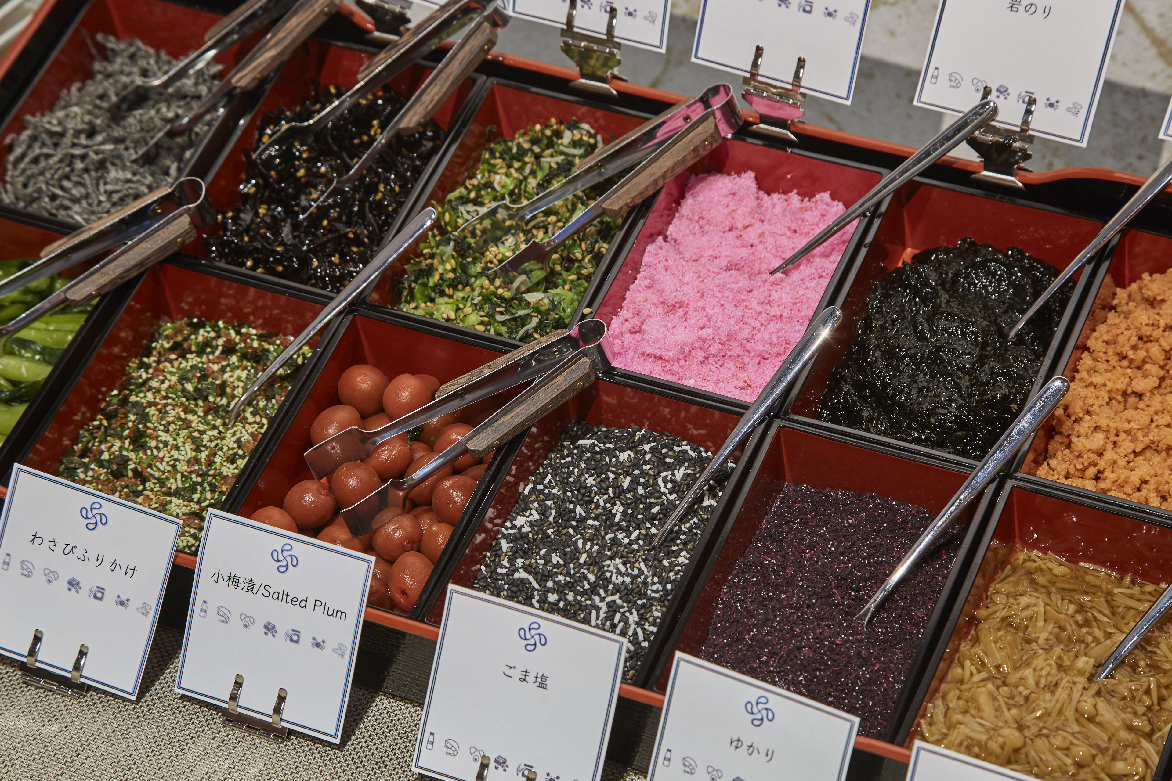 A variety of food items in containers with tongs, each labeled with Japanese text.