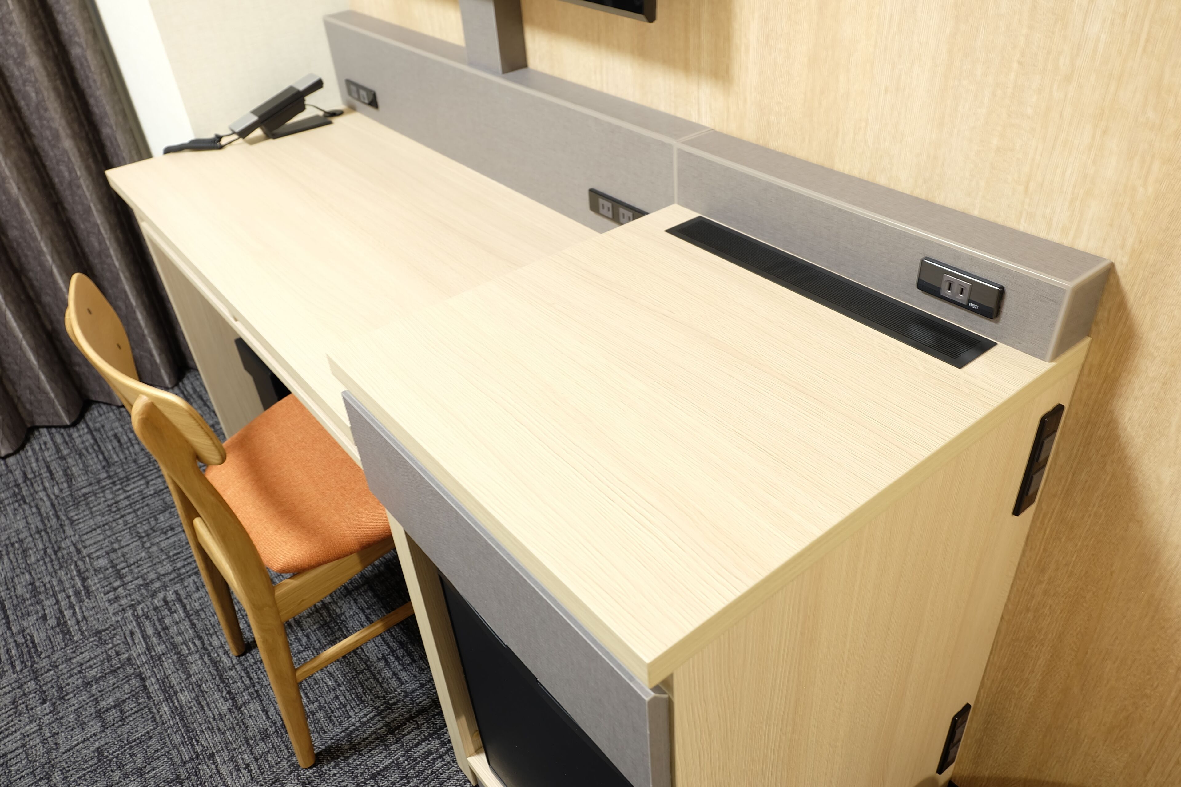 A hotel workspace with a wooden desk, a cushioned chair, and a built-in charging station.