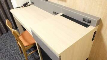 Un espacio de trabajo en hotel con un escritorio de madera, una silla acolchada y una estación de carga integrada.