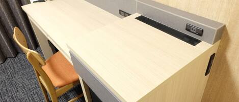 A hotel workspace with a wooden desk, a cushioned chair, and a built-in charging station.