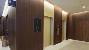 A modern elevator area with wooden paneling and a digital floor indicator. - Iroha Grand Hotel (Matsumoto)