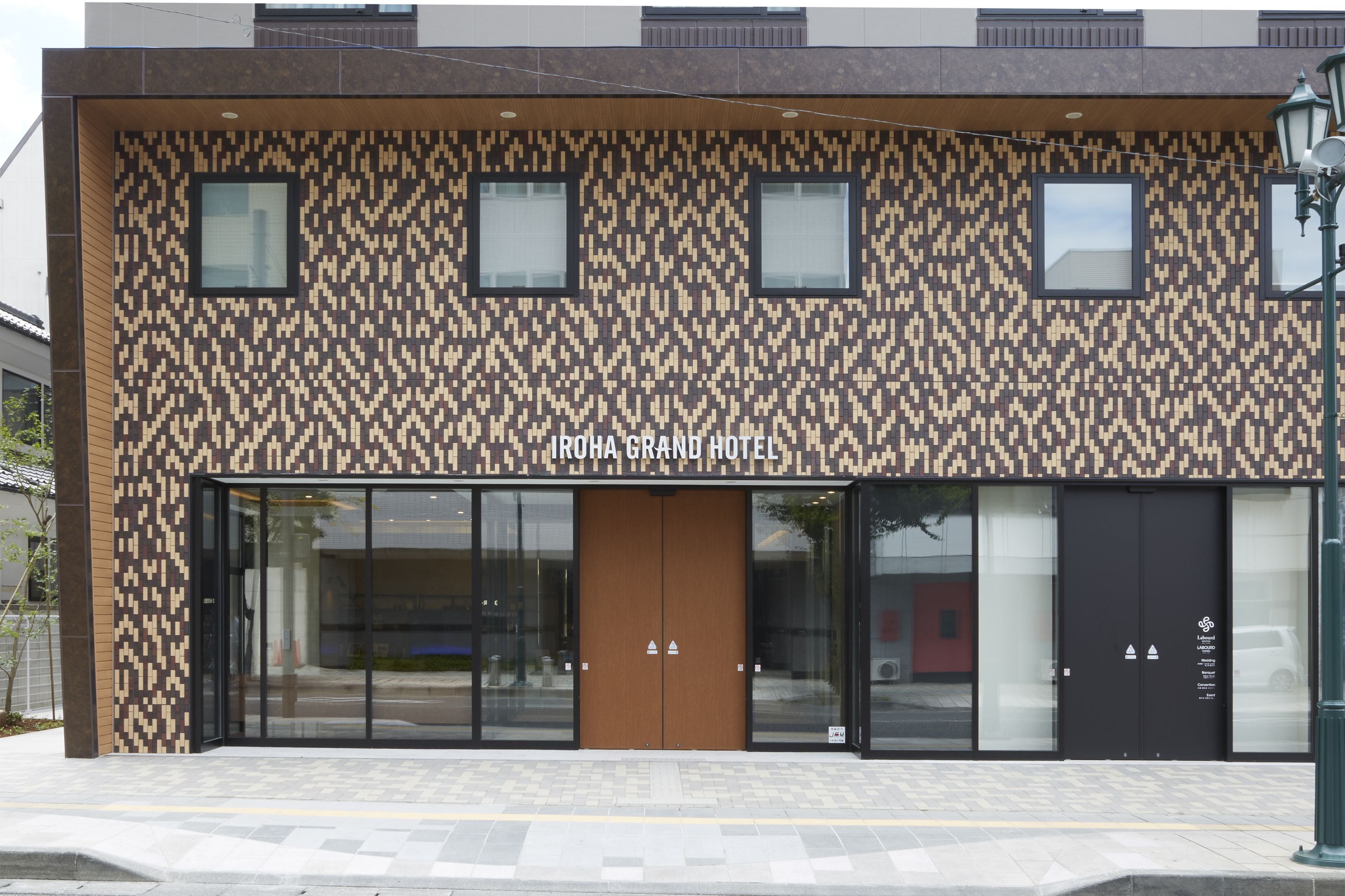 A modern building with a patterned facade, large glass doors, and a sign reading "IROHA GRAND HOTEL".