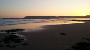 Une plage au coucher du soleil, avec des vagues et des falaises qui se dessinent à l’horizon.