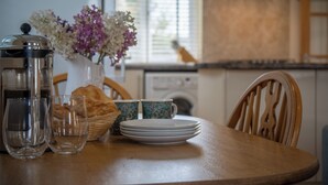 Une table de salle à manger en bois, avec une machine à café, des verres, des assiettes et un panier de pain.