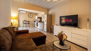 Un soggiorno moderno con un divano marrone, una TV che mostra 'NETFLIX', una cucina sullo sfondo e un'area pranzo.