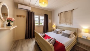 Una camera d'albergo con un letto, lampade sui comodini, uno specchio, una finestra con tende e un condizionatore d'aria.