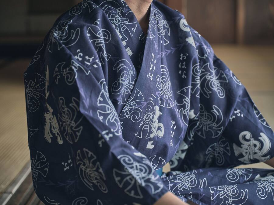A person seated on a tatami mat, wearing a dark blue kimono with white patterns.