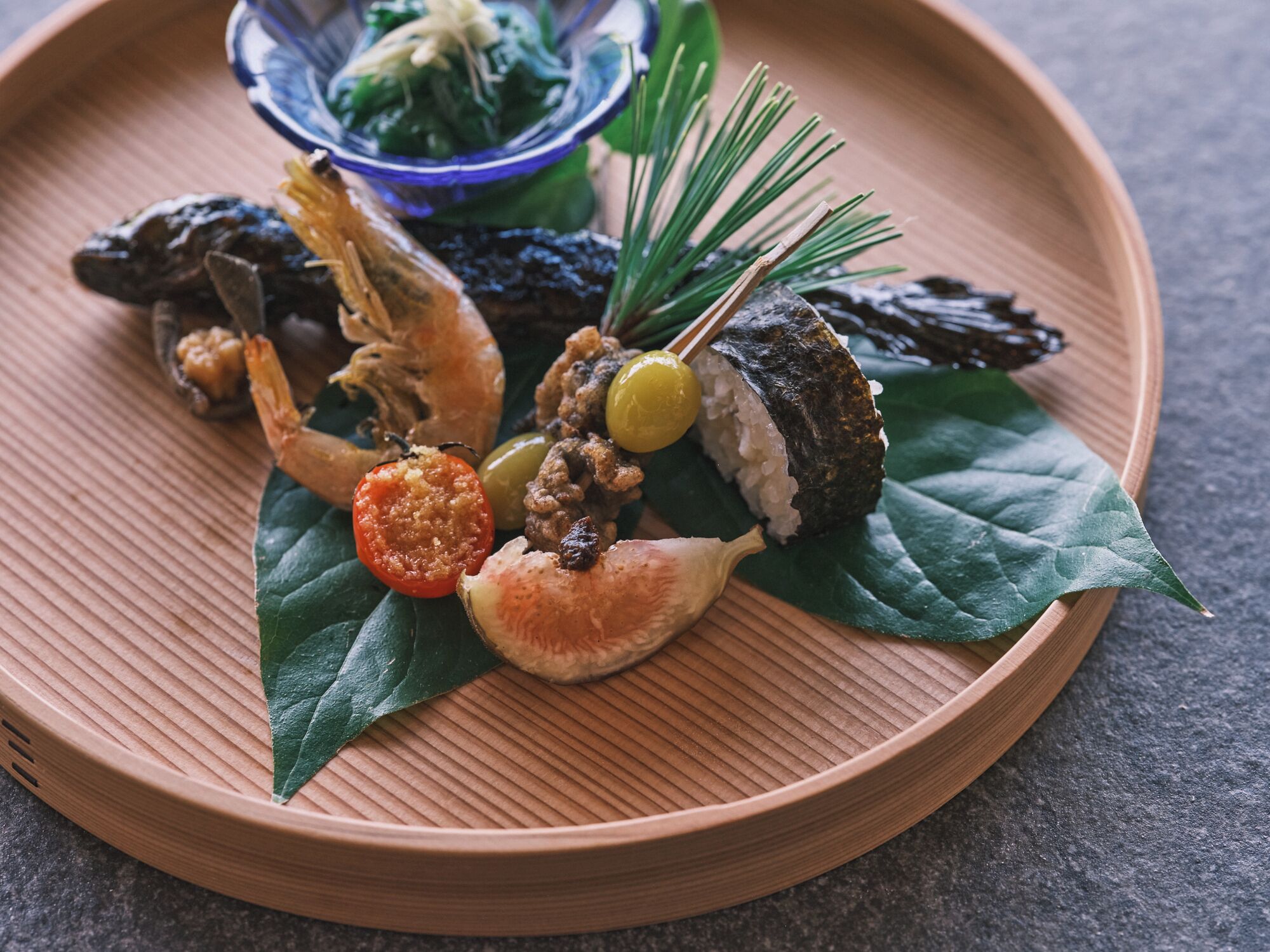 A wooden tray with various Japanese dishes including sushi, vegetables, and seafood.