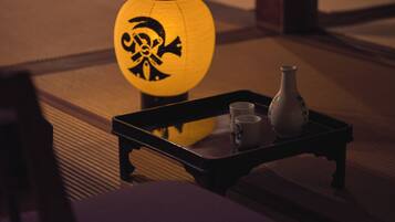 A traditional Japanese room with tatami flooring, a black lacquered table with two cups and a vase, and a yellow lantern with a black design.