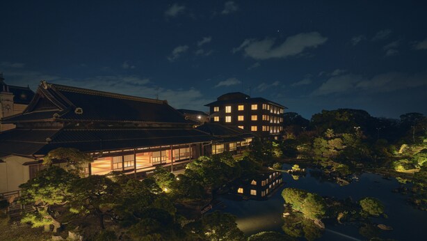 Un bâtiment japonais traditionnel à plusieurs étages, entouré d’un étang et d’arbres.