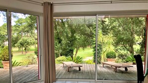 A room with large sliding glass doors leading to an outdoor deck with two wooden loungers and a chair.