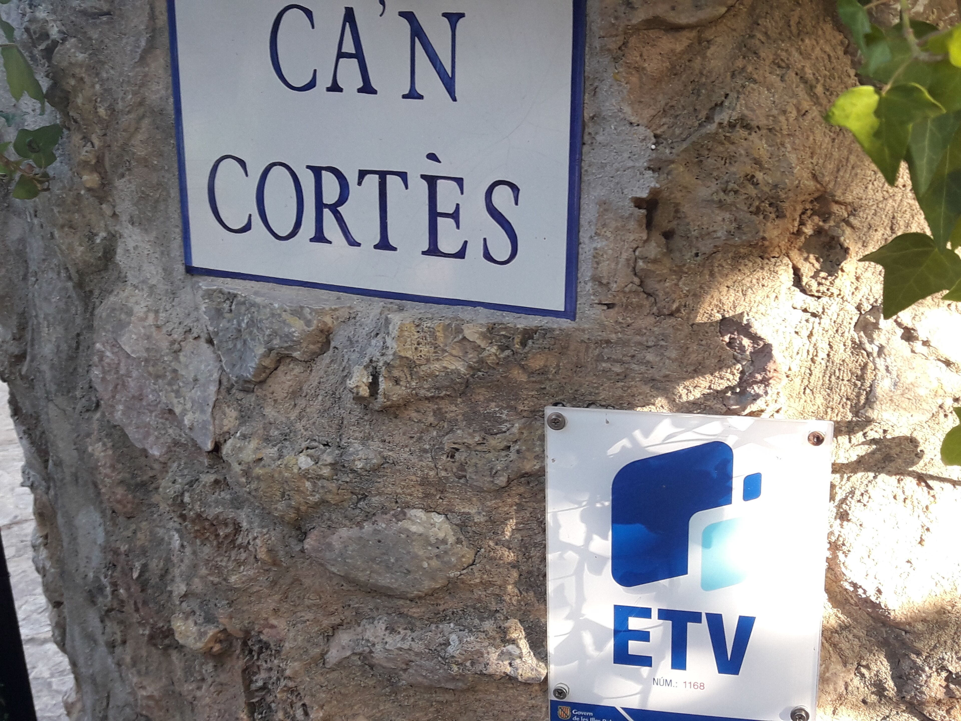Un muro in pietra con due cartelli, uno con la scritta 'CAN CORTES' e l'altro 'ETV' con il numero '1168'.