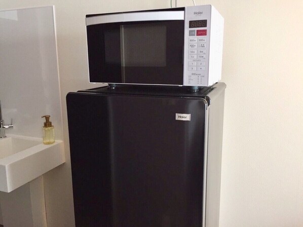 A black refrigerator with a microwave on top, a white sink, and a soap dispenser.