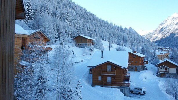 Un villaggio montano innevato con case di legno e cielo sereno.