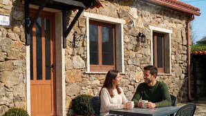 A stone building with a tiled roof, a wooden door, and two windows. There is a table with chairs outside. - Galician Stone Cottage for 2 people  (A Coruna)