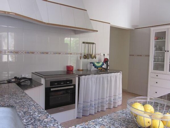 A kitchen with white cabinets, a stove, and a sink. There is a metal basket with lemons on the counter.