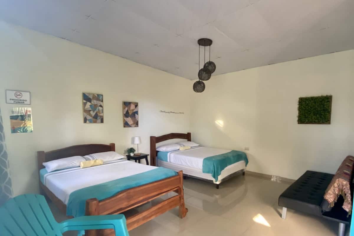 Habitación de hotel con dos camas, un sofá pequeño, una silla y una lámpara en el techo.