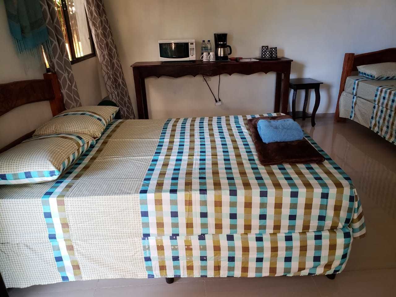A bedroom with two beds, a wooden headboard, a bedside table with a microwave, a coffee maker, and a small table.
